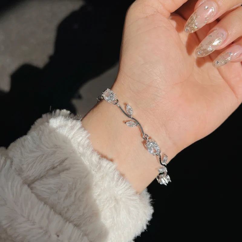 Hand wearing a silver bracelet with floral design against a dark background